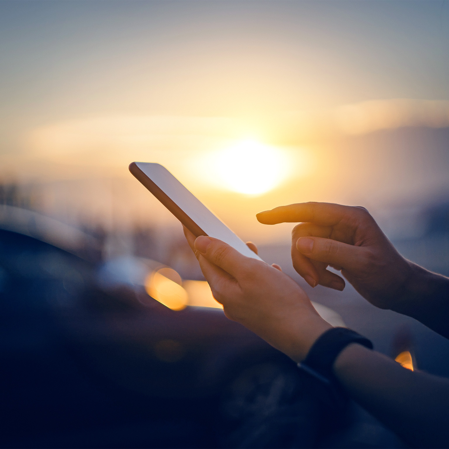 Close-up of woman's hand typing on a smartphone in the city in front of cars at beautiful sunset