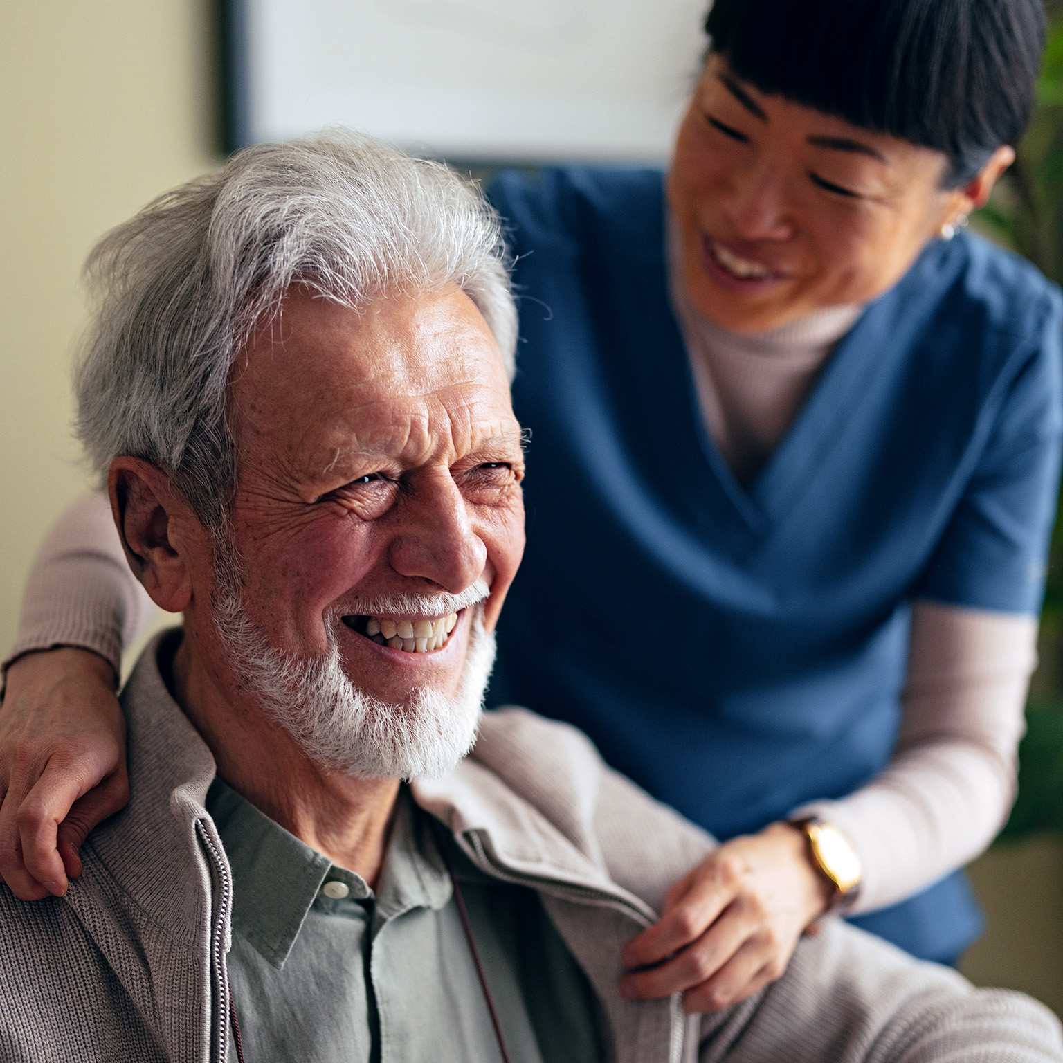 Portrait of a Smiling Elderly Man Taking a Jacket off With a Help of a Woman in a Care Home