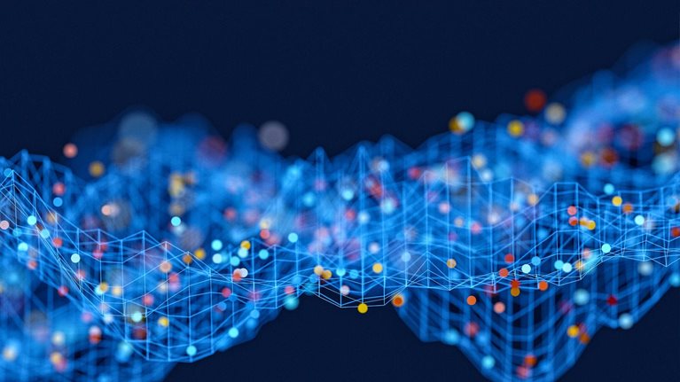 An abstract rendering of a data wave, with interconnected blue lines forming a grid-like structure. Spheres in shades of red, yellow, and blue, representing data points within raw data sets, are distributed across this grid, set against a solid dark blue background.