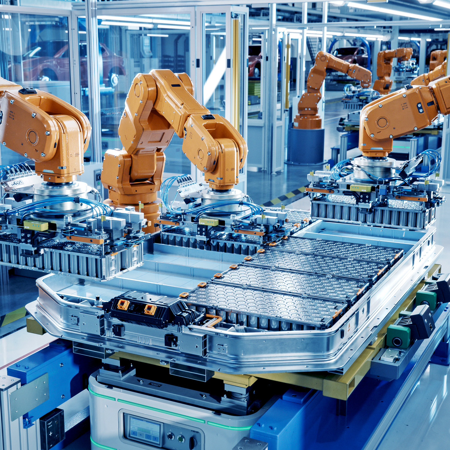 A modern factory floor where multiple orange industrial robotic arms are assembling large battery packs on an automated production line. The environment is clean, brightly lit, and highly organized, emphasizing advanced manufacturing and automation technology.