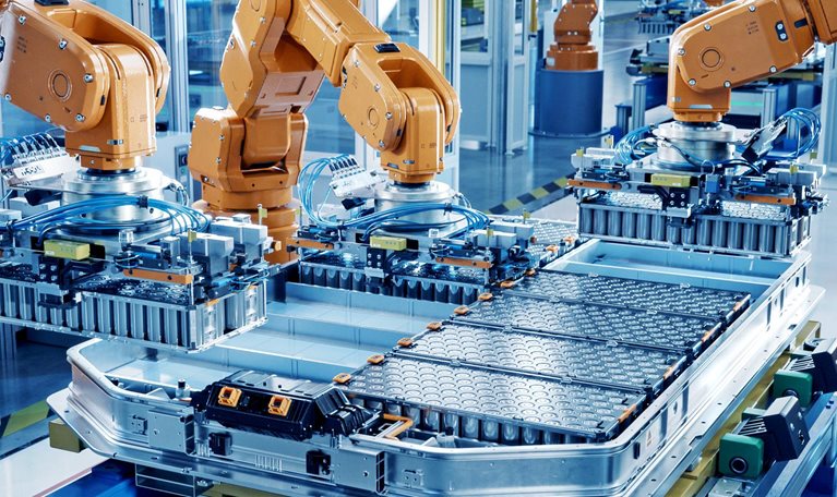 A modern factory floor where multiple orange industrial robotic arms are assembling large battery packs on an automated production line. The environment is clean, brightly lit, and highly organized, emphasizing advanced manufacturing and automation technology.