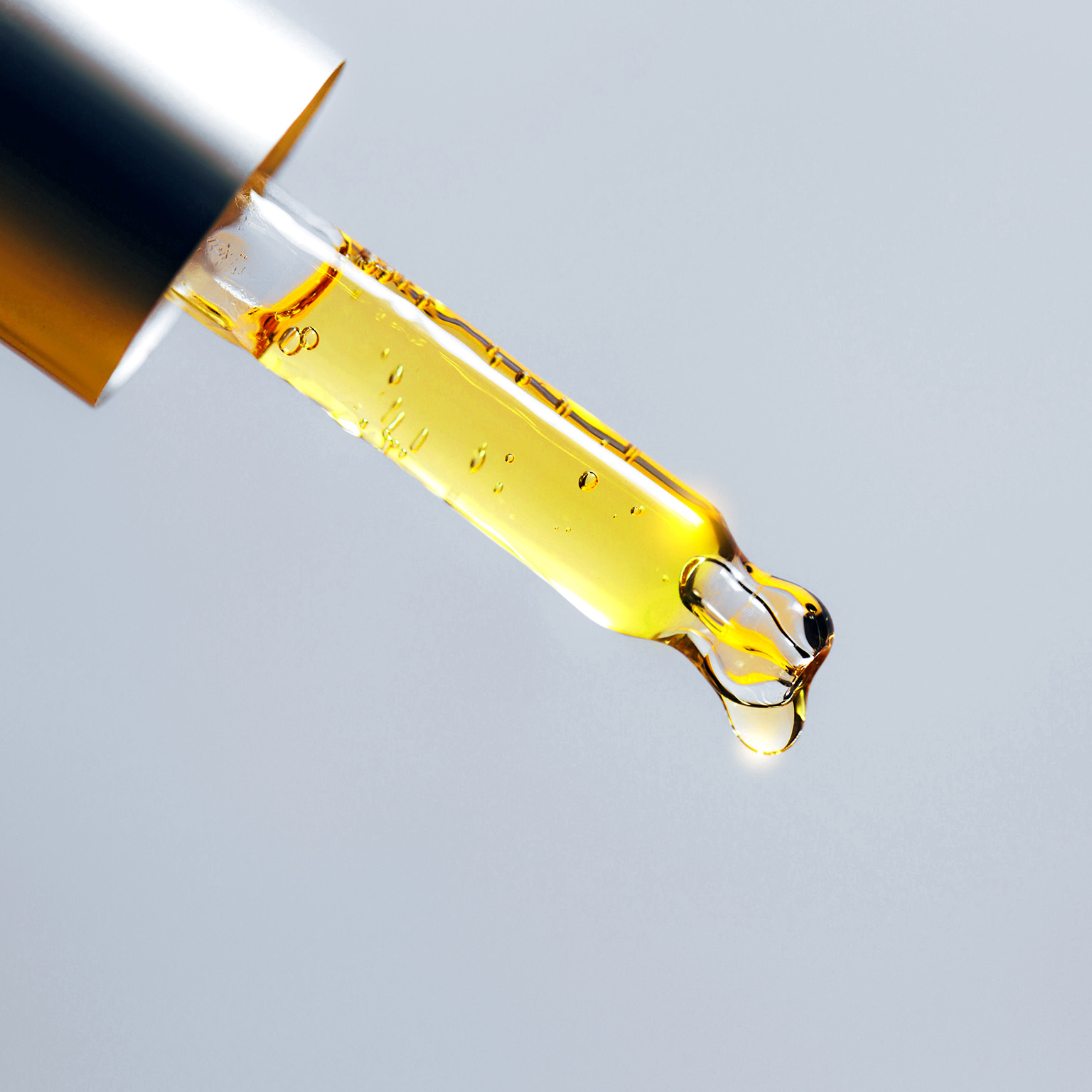 Closeup pipette dripping fragrant oil for cosmetic or spa procedure against grey background