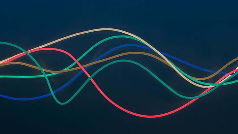 Blue, green, red, brown and white wire in wave pattern on dark blue background - stock photo