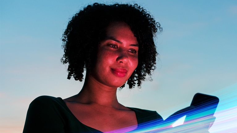 Woman using a smartphone against a vibrant blue sky backdrop, surrounded by vivid streaks of colorful light.