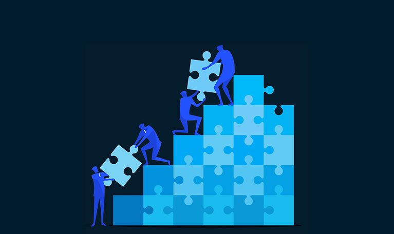 A flat-style digital illustration shows four blue human figures working together to build an ascending staircase of interlocking jigsaw puzzle pieces in shades of blue and cyan. A figure at the base lifts a light blue puzzle piece up to another figure leaning down from a lower step, while higher up a kneeling figure passes a piece to a figure standing at the top, who fits it into the tallest column. The scene is set against a dark navy background. End of image description.