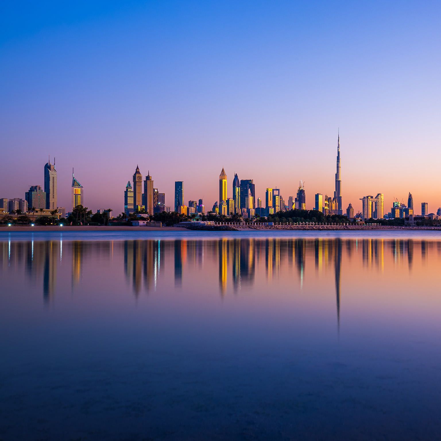 Beautiful sunset showing the Dubai Skyline with mirrorlike reflections in the lake - stock photo