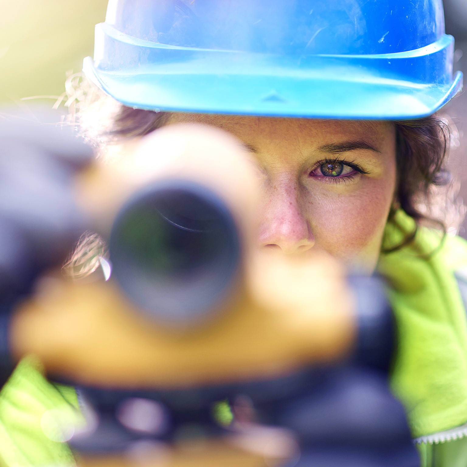 Close up of young female surveyor looking through the lens of a theodolite checking levels on a site.