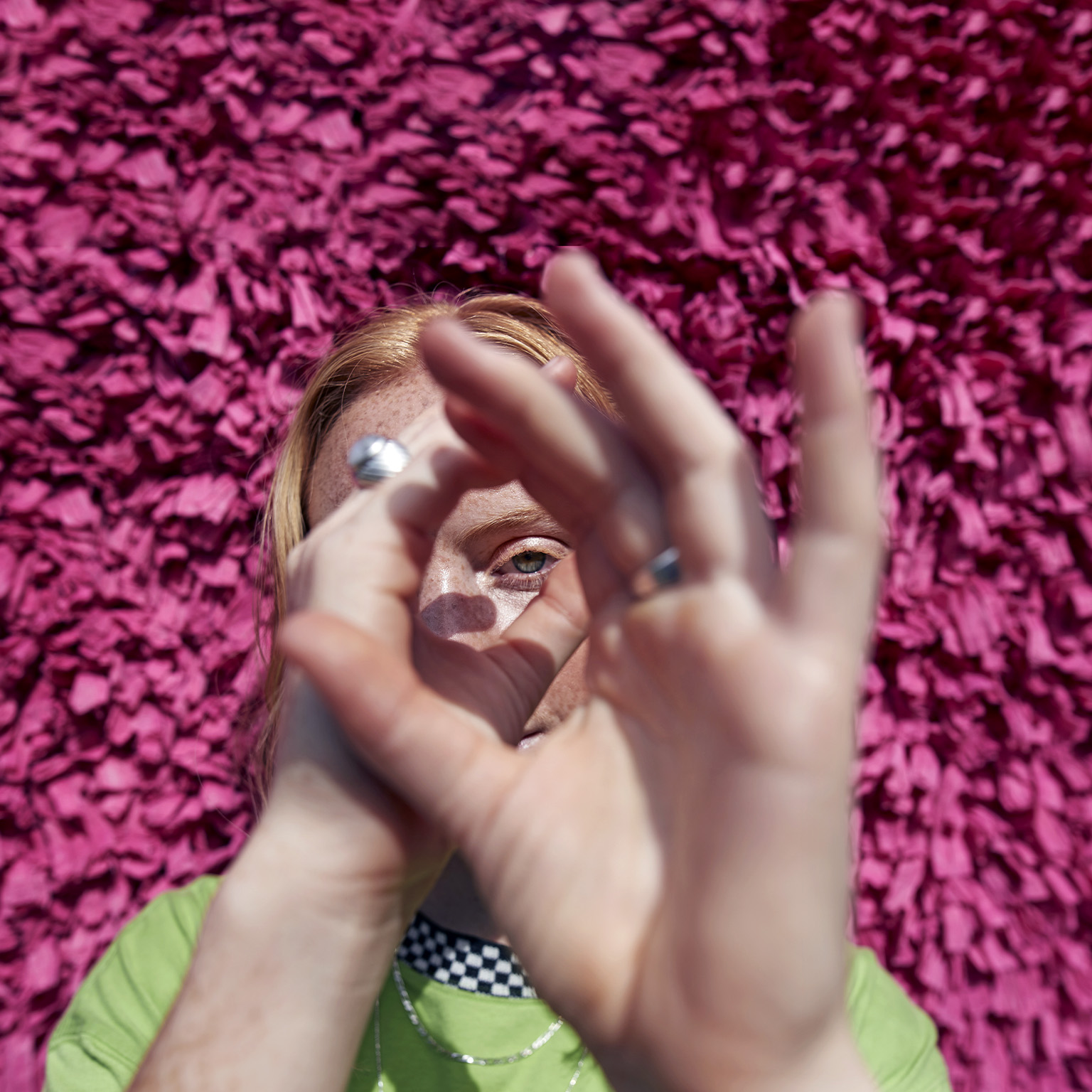 Image of a woman looking through her hands like a telescope with a textured wall behind her.