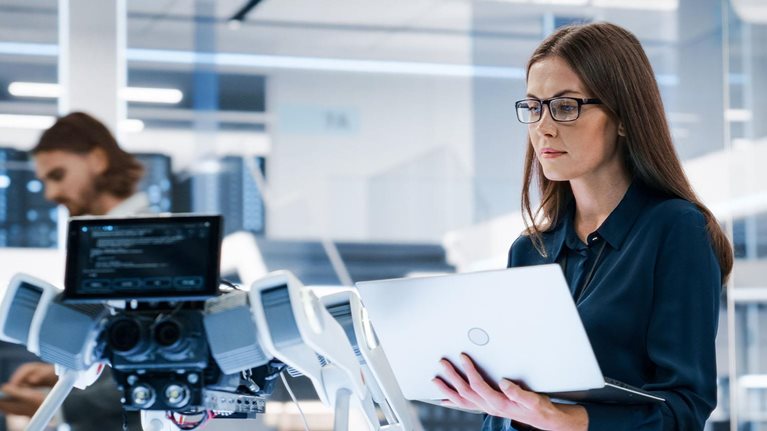 Portrait of a Young Robotics Engineer Using Laptop Computer, Analyzing Robotic Machine Concept in a High Tech Factory.