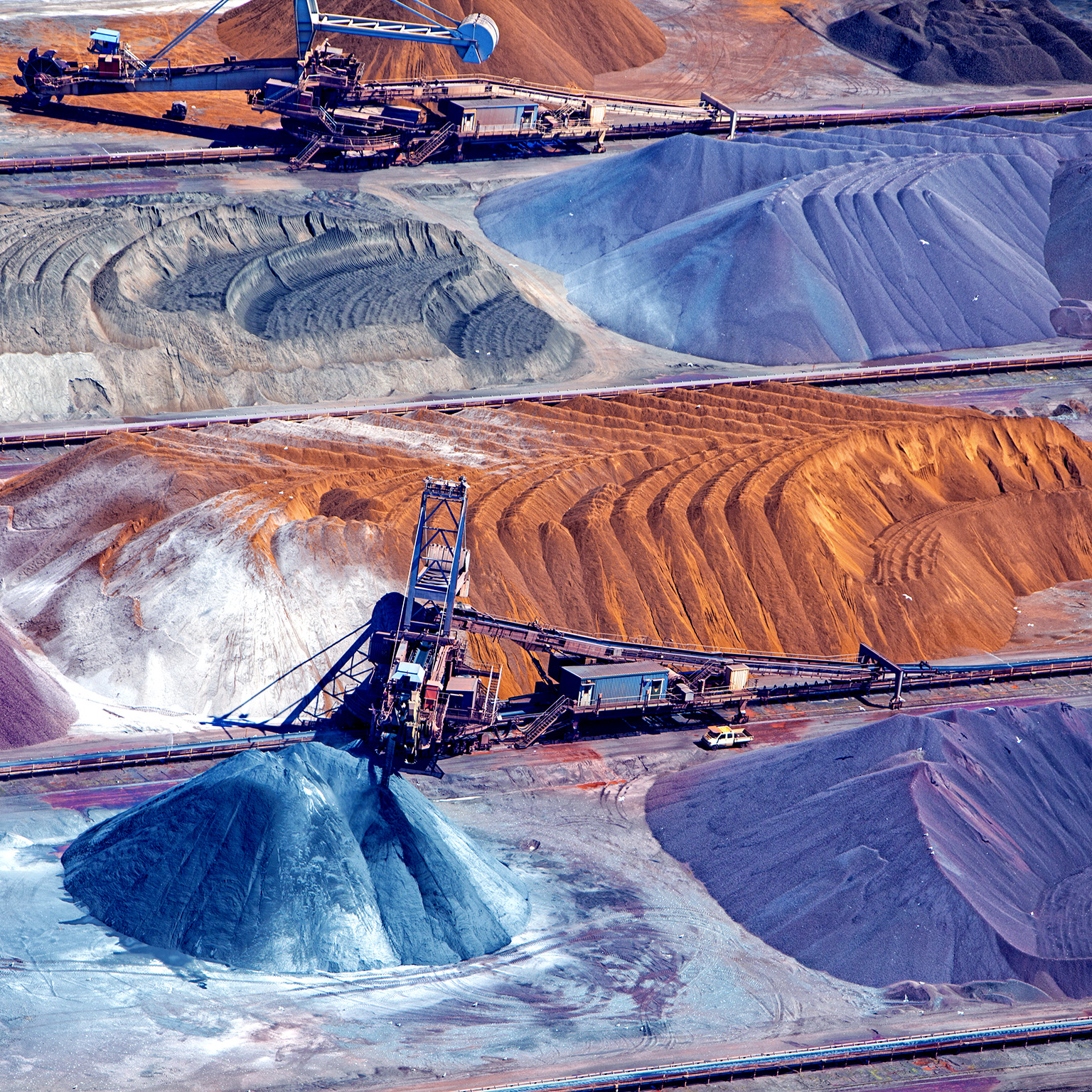 An aerial image of a piles of ore organized around a conveyor belt.
