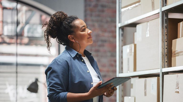 Portrait of a Manager Checking Inventory, Writing in Tablet Computer. Black Woman Working in a Warehouse Storeroom with Rows of Shelves Full of Parcels, Packages with Orders Ready for Shipment. - stock photo