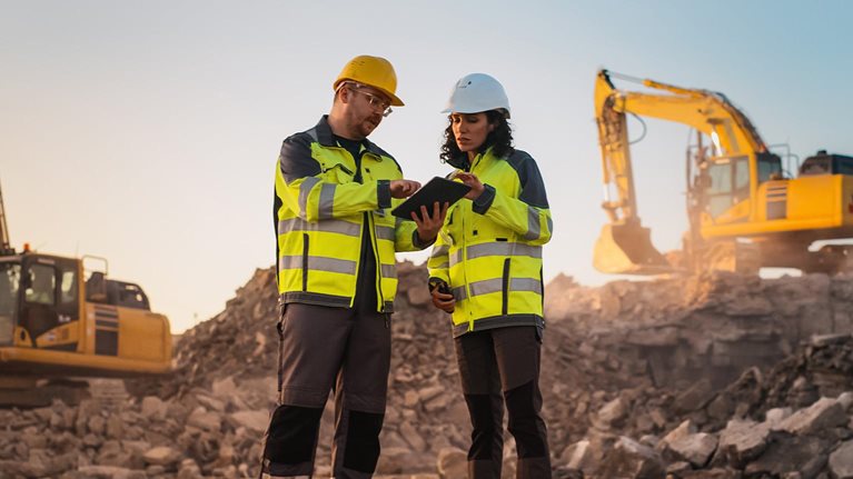 Using Tablet On Construction Site of New Apartment Complex. Real Estate Developers Discussing Business, Excavators Working.