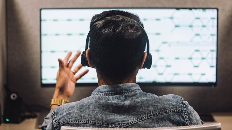 Rear view of young male customer service executive talking through headset sitting at desk in illuminated call center