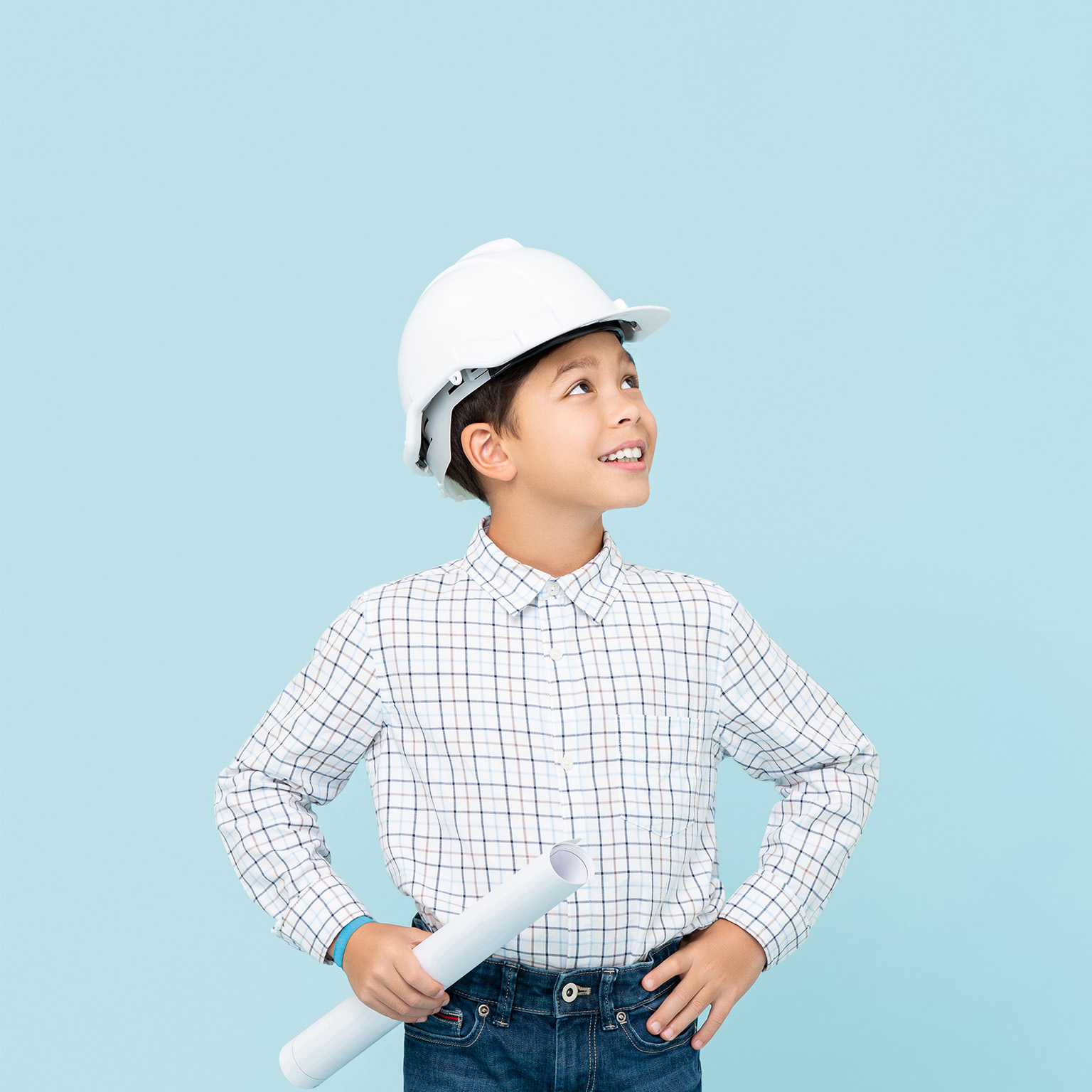 Smiling young boy aspiring to be future engineer wearing white hard hat and holding blueprint - stock photo