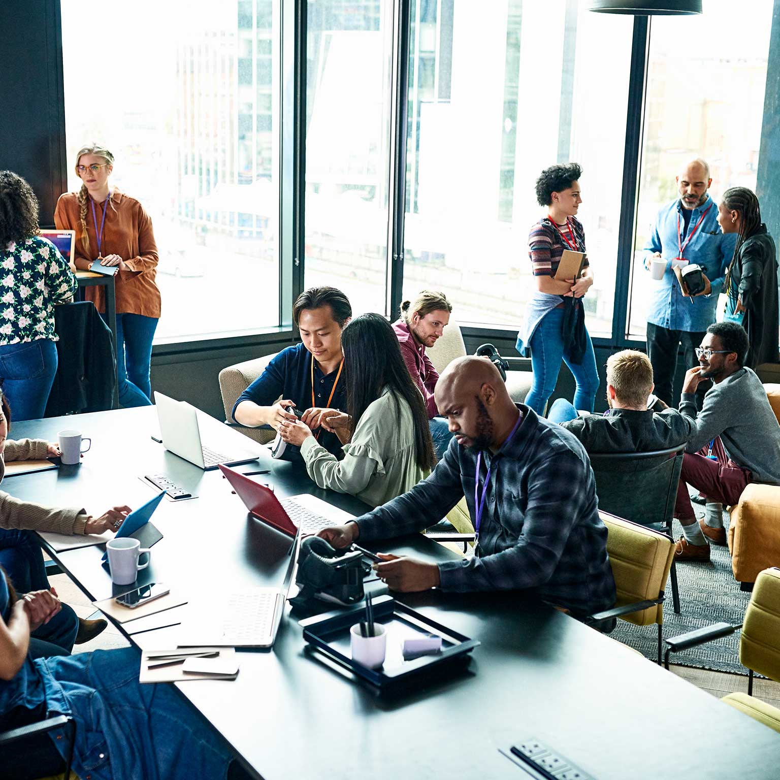 Multiple small groups of people working and congregating in a large office space 