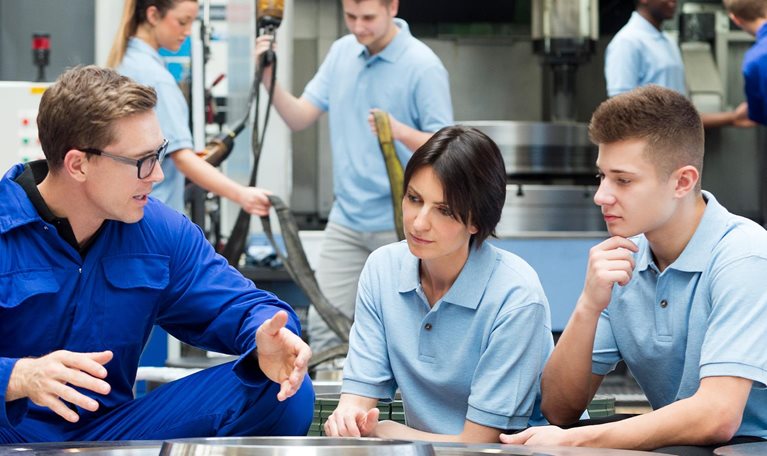 Three factory workers in workspace talking.