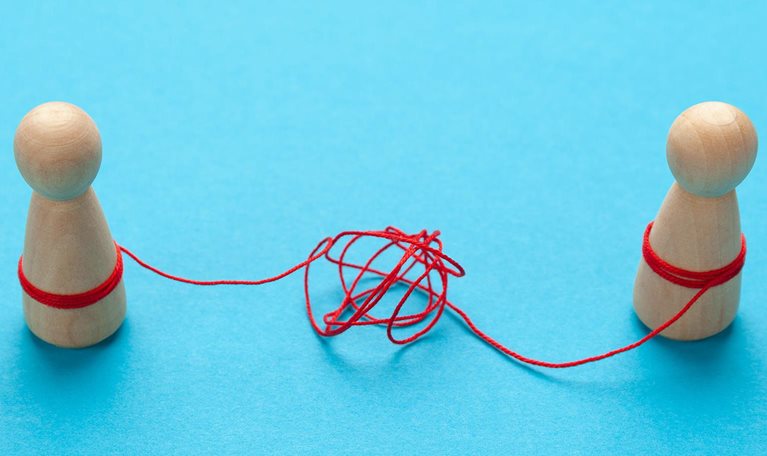 Confused relationships of people in a couple. Two wooden block figures tied together by string tangled in knots.