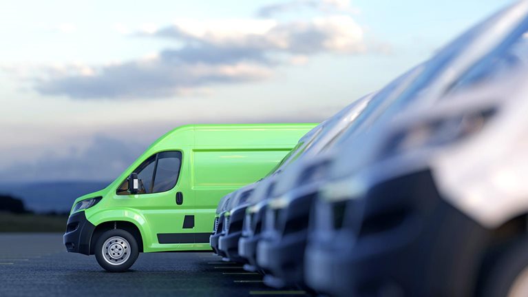 Image of a modern green electric van standing out from a row of other plain white vans.