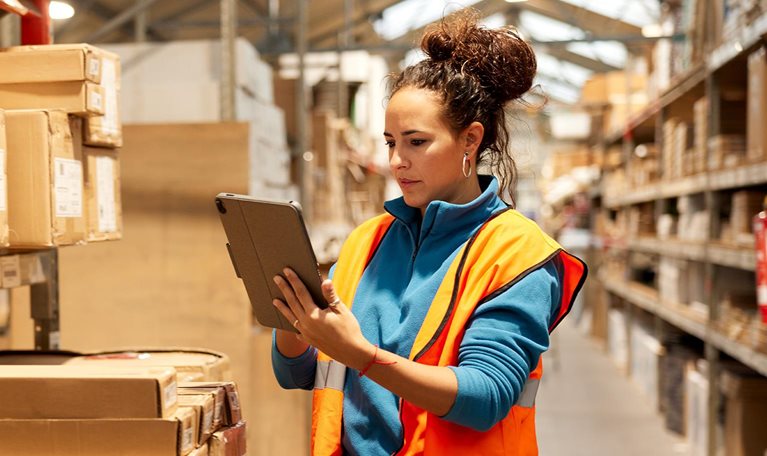 A warehouse worker takes inventory in the storage room standing next to a shelf and using a digital tablet. - stock photo