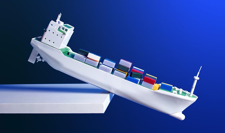 An conceptual image of a toy container ship with multi-colored containers teetering on the edge of a shelf.