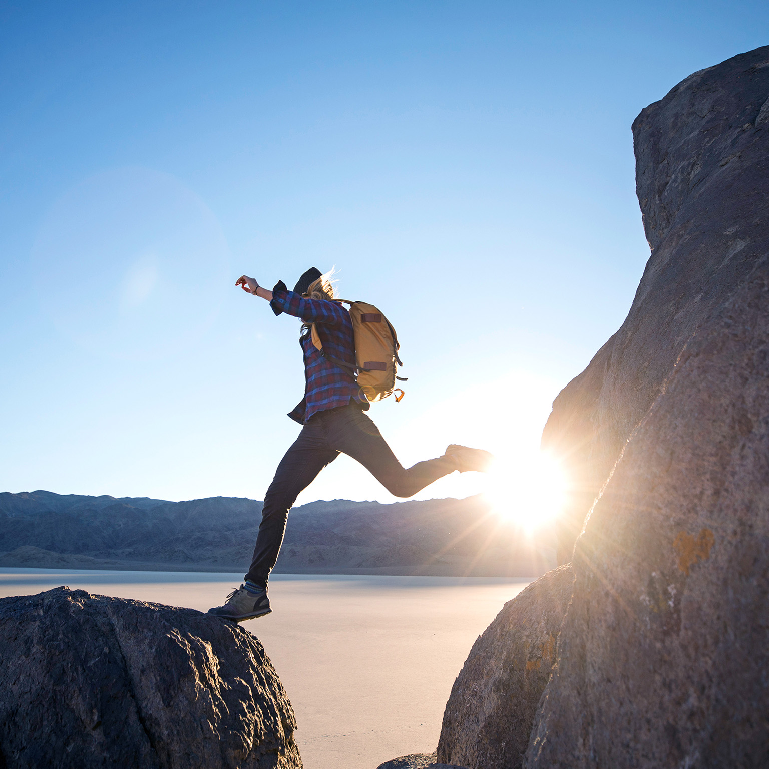 A woman jumps from one large rock to another while hiking in The Racetracks region of Death Valley.
