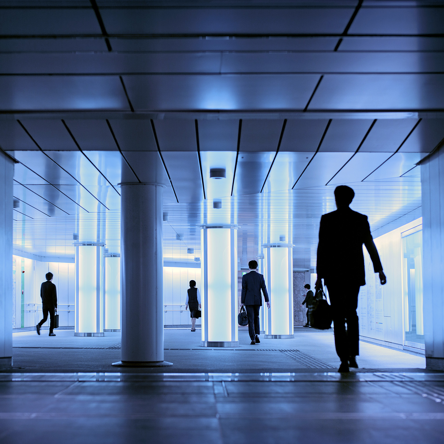 Silhouettes of people walking in a well lit hallway