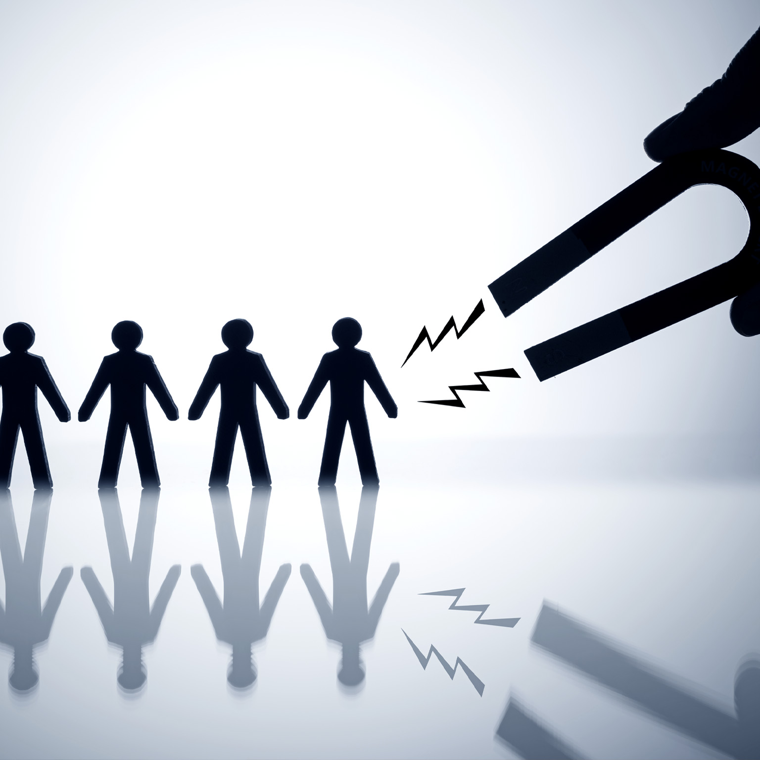 A hand holding a horseshoe magnet trying to attract a row of figures in the shape of people. 