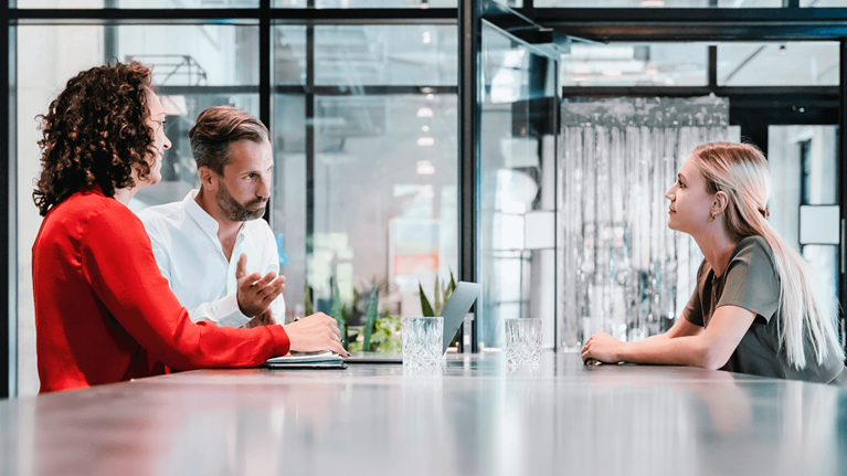 Three people converse at a desk