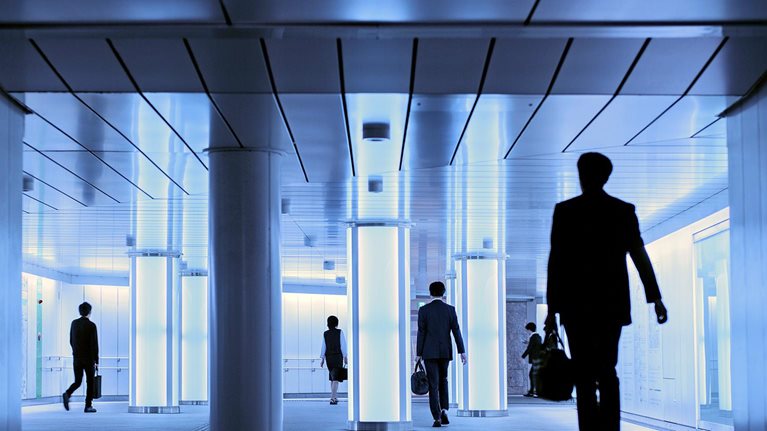 Silhouettes of people walking in a well lit hallway