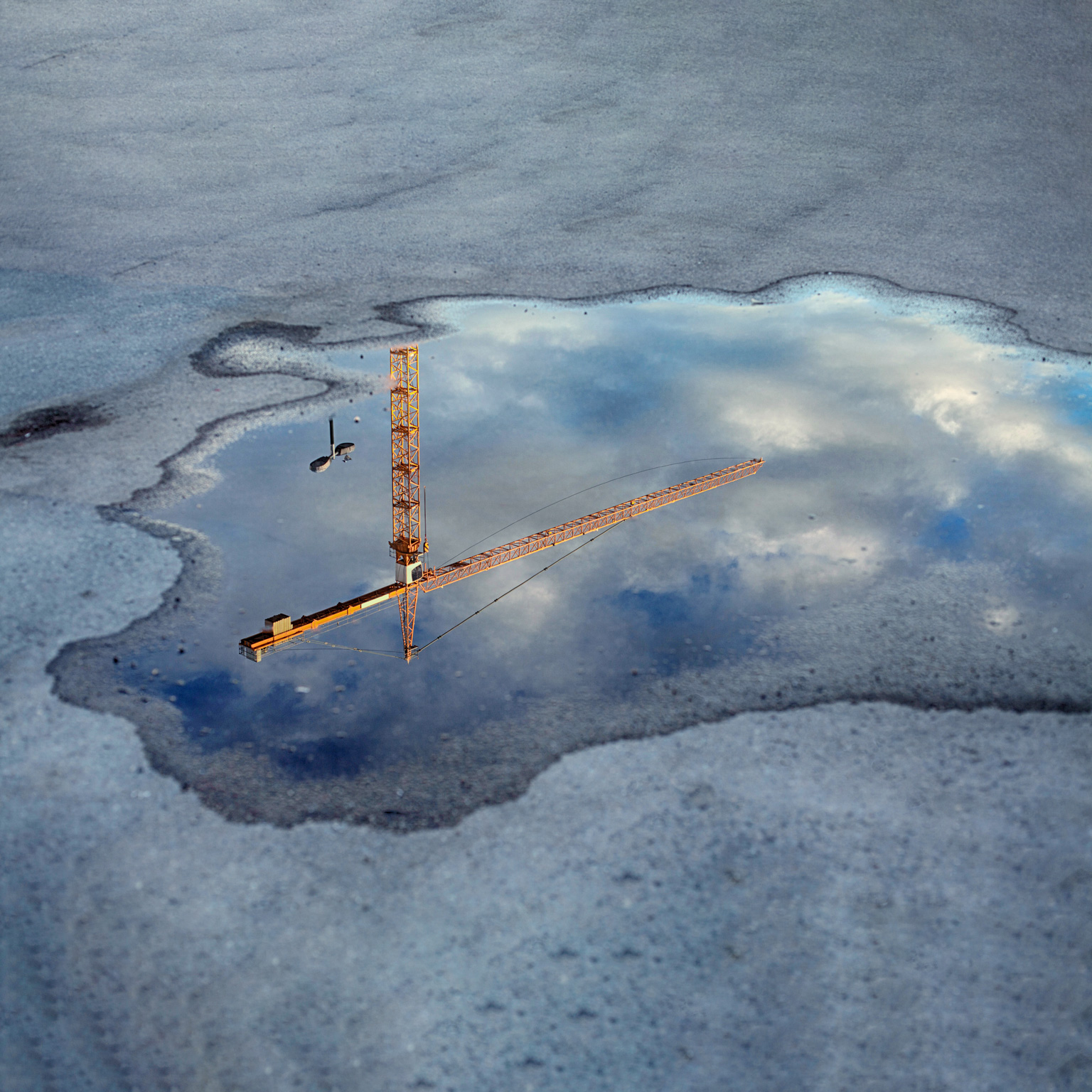 Reflection of a crane tower in a puddle