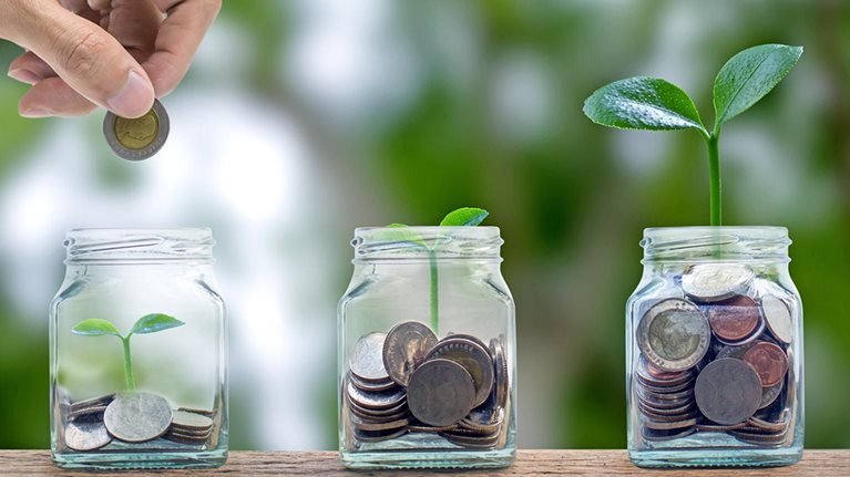 A hand putting a coin into a glass bottle containing coins