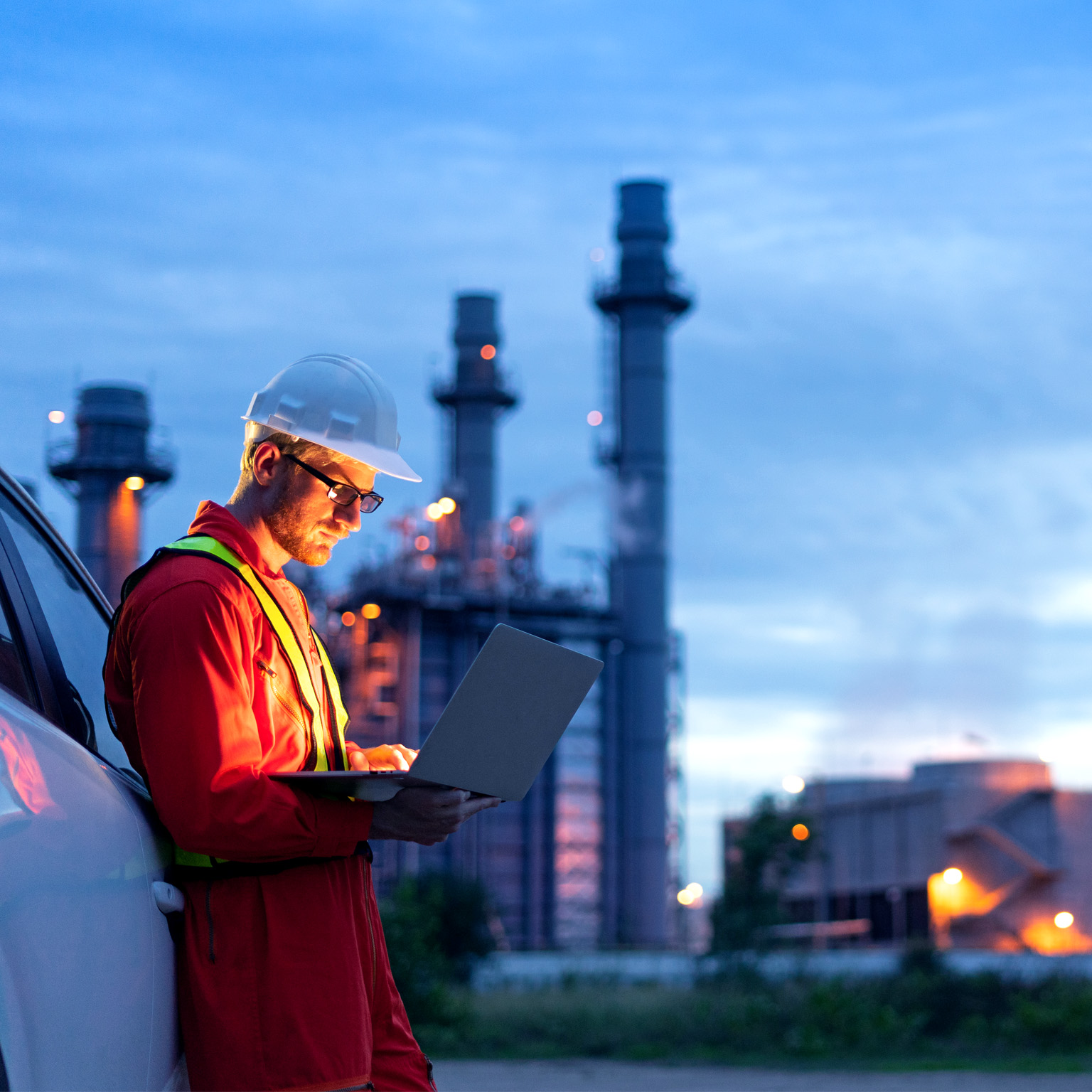 Engineer wearing safety helmet using laptop with oil refinery background