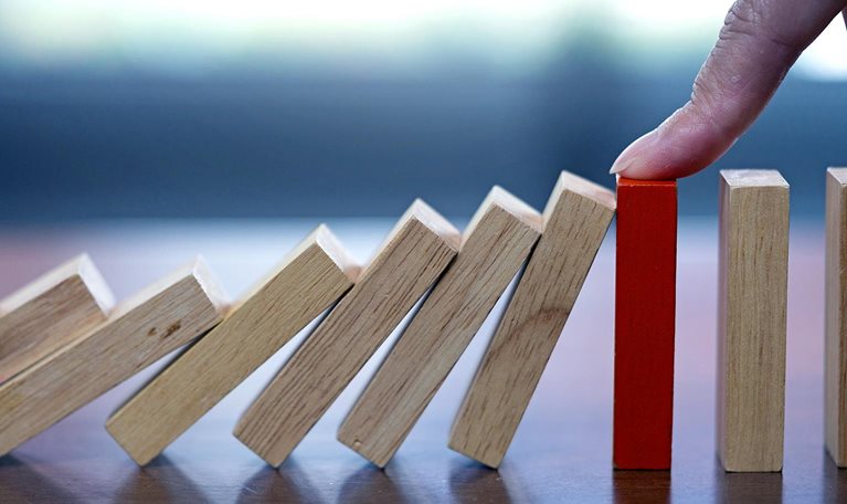 Close up image of a finger reaching down and stopping falling dominos.
