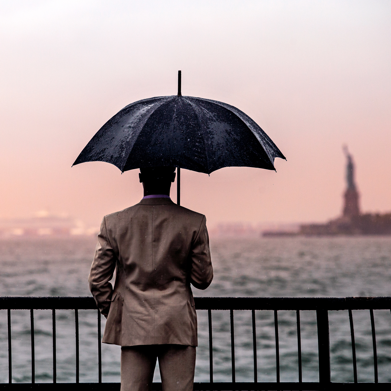 Rear view of man with umbrella standing by railing against sea.
