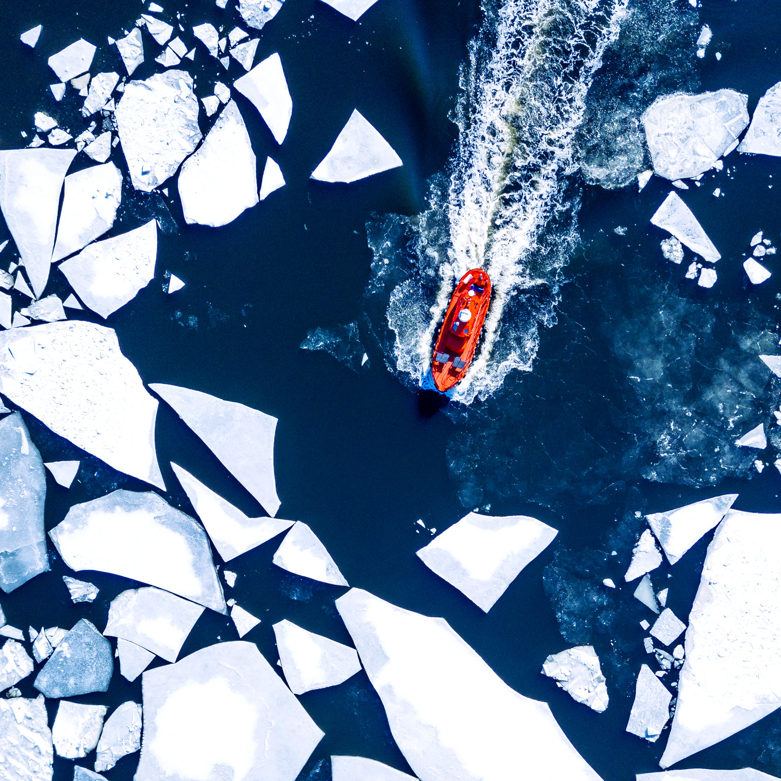 Wintery aerial view of a red ice-breaker ship pushing through cracked sea ice