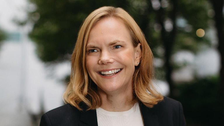 Portrait of a smiling Janet Bannister with an outdoor setting as a blurred background.