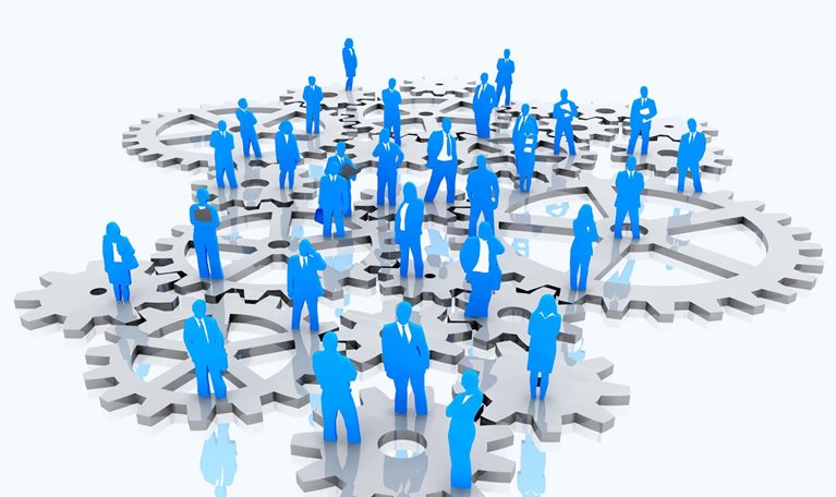 An isometric illustration features a group of individuals dressed in business attire standing on interlocking gears. The people are depicted in blue, while the gears are silver.