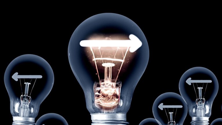 A group of light bulbs set on a dark backdrop. All of the bulbs display a left-facing arrow, except for one bulb that stands out with a right-facing arrow and is illuminated.