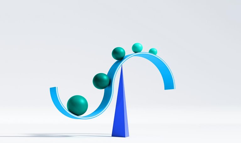 A curved, cyan structure resembling a sideways S is balanced atop a dark blue pyramid. Along the curve of the structure, there are several spheres of varying sizes, starting from the largest and descending in size as they move to a higher point on the curve.