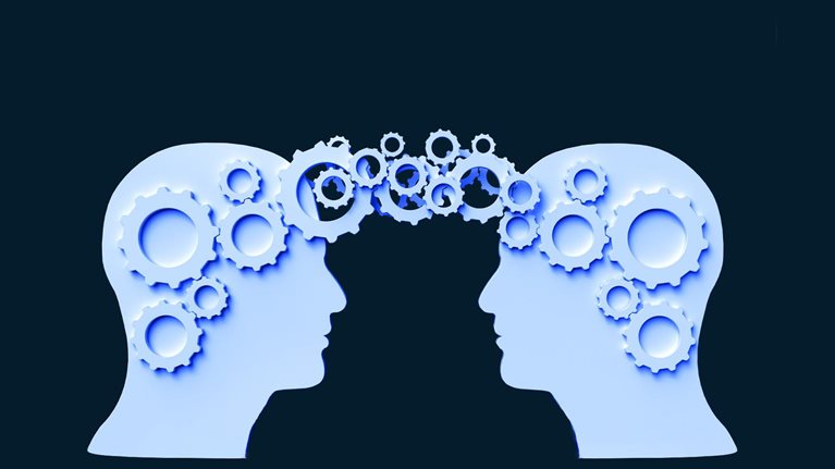 Two silhouettes of human heads face each other against a dark background. Gears of various sizes connect between the two heads, symbolizing the exchange of ideas and collaboration.