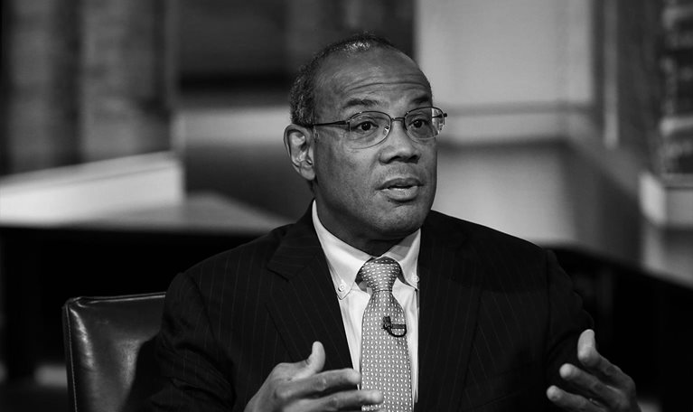 Black and white Portrait of John Rogers in a library appearing to be making a point in a discussion.