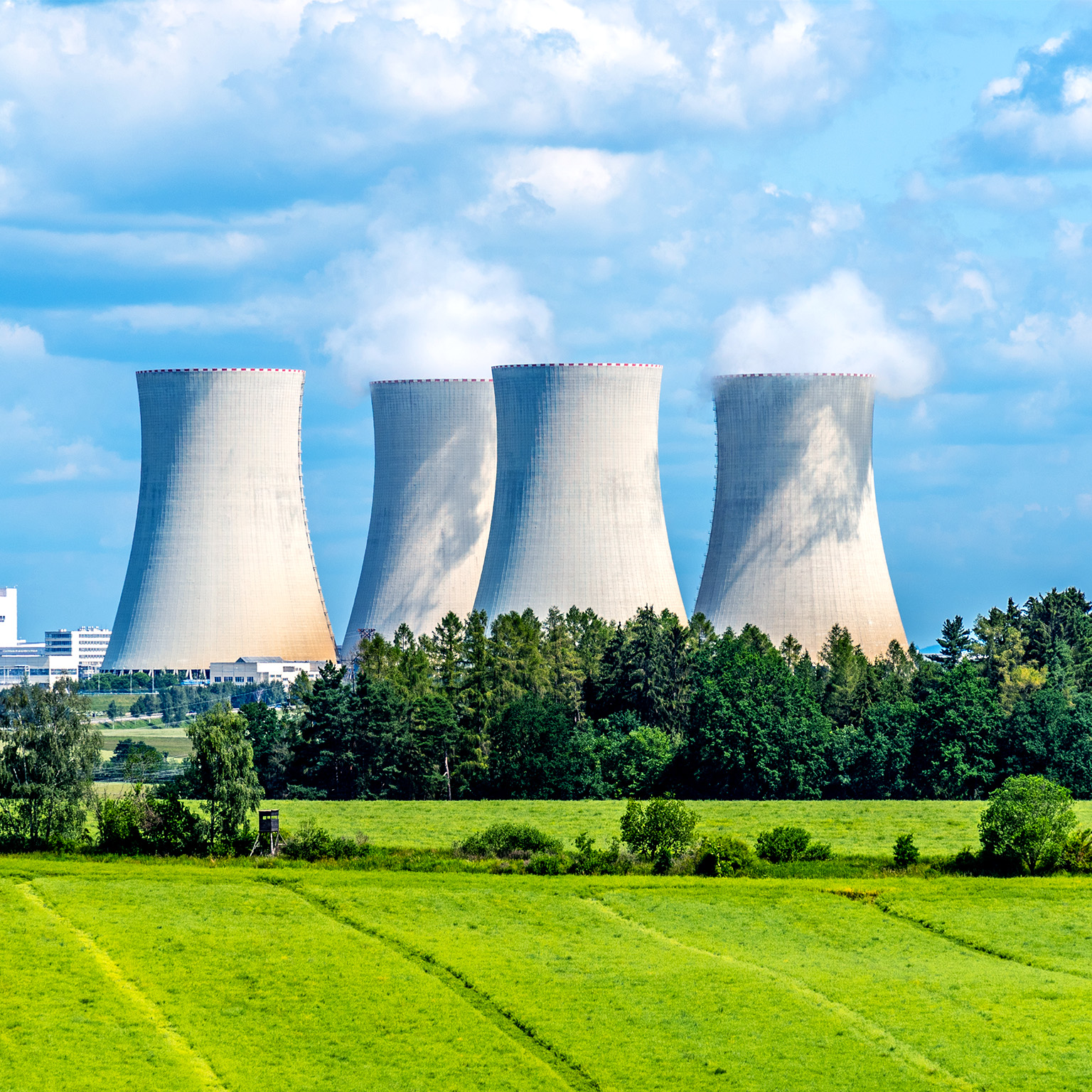 Nuclear power plant with trees and a lush green field in front of it