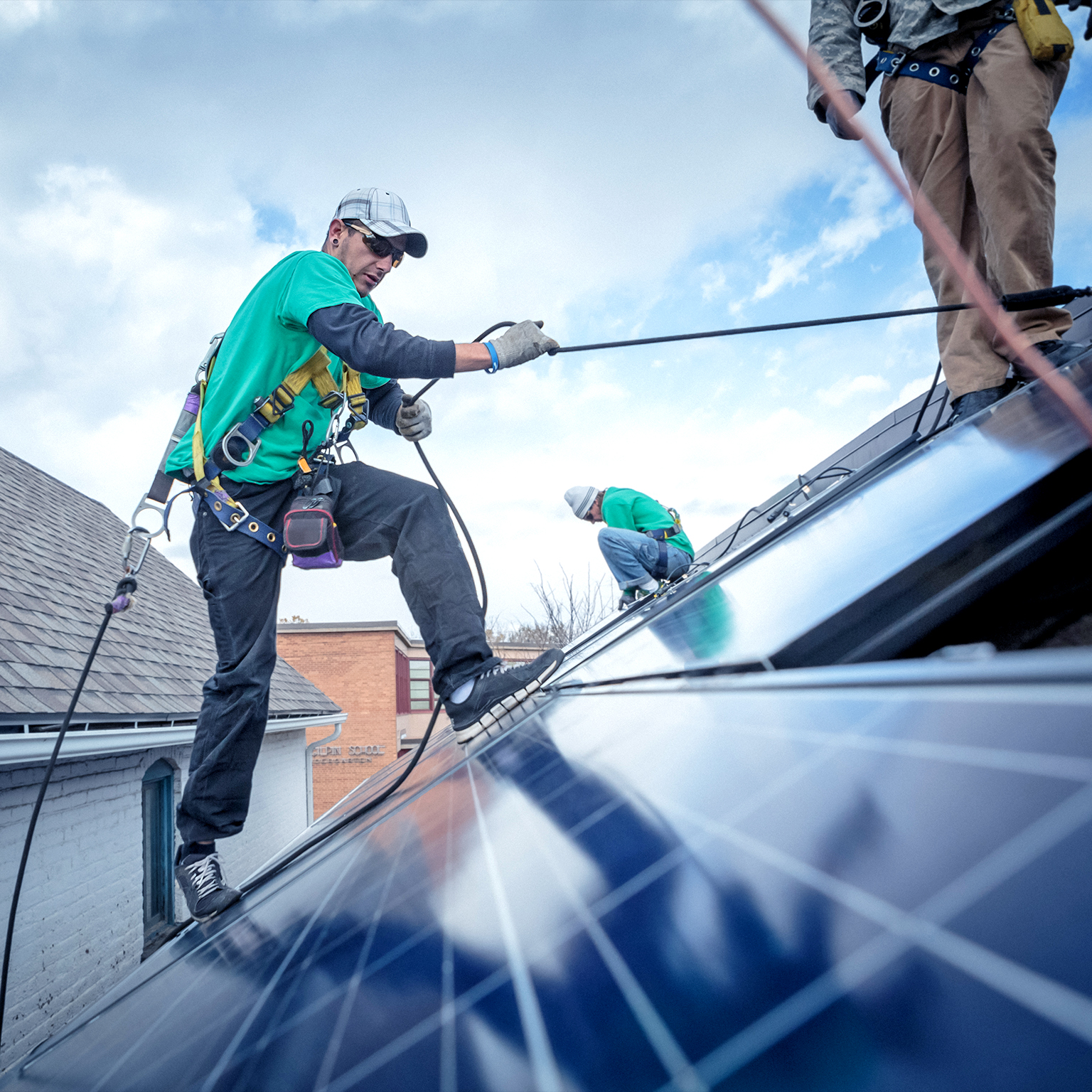 Construction worker uses safety roles to move around a roof with solar panels in the foreground