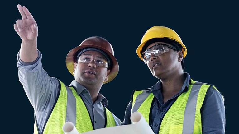 Image of a Latino man and woman construction workers looking and pointing up and away while discussion floor plans.