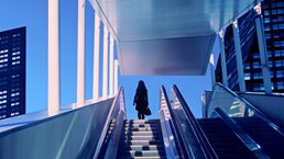 Early evening at modern business district with silhouette of businesswoman on top of a moving escalator.
