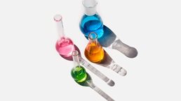 Laboratory glassware containing liquids of different colors on a light gray background.