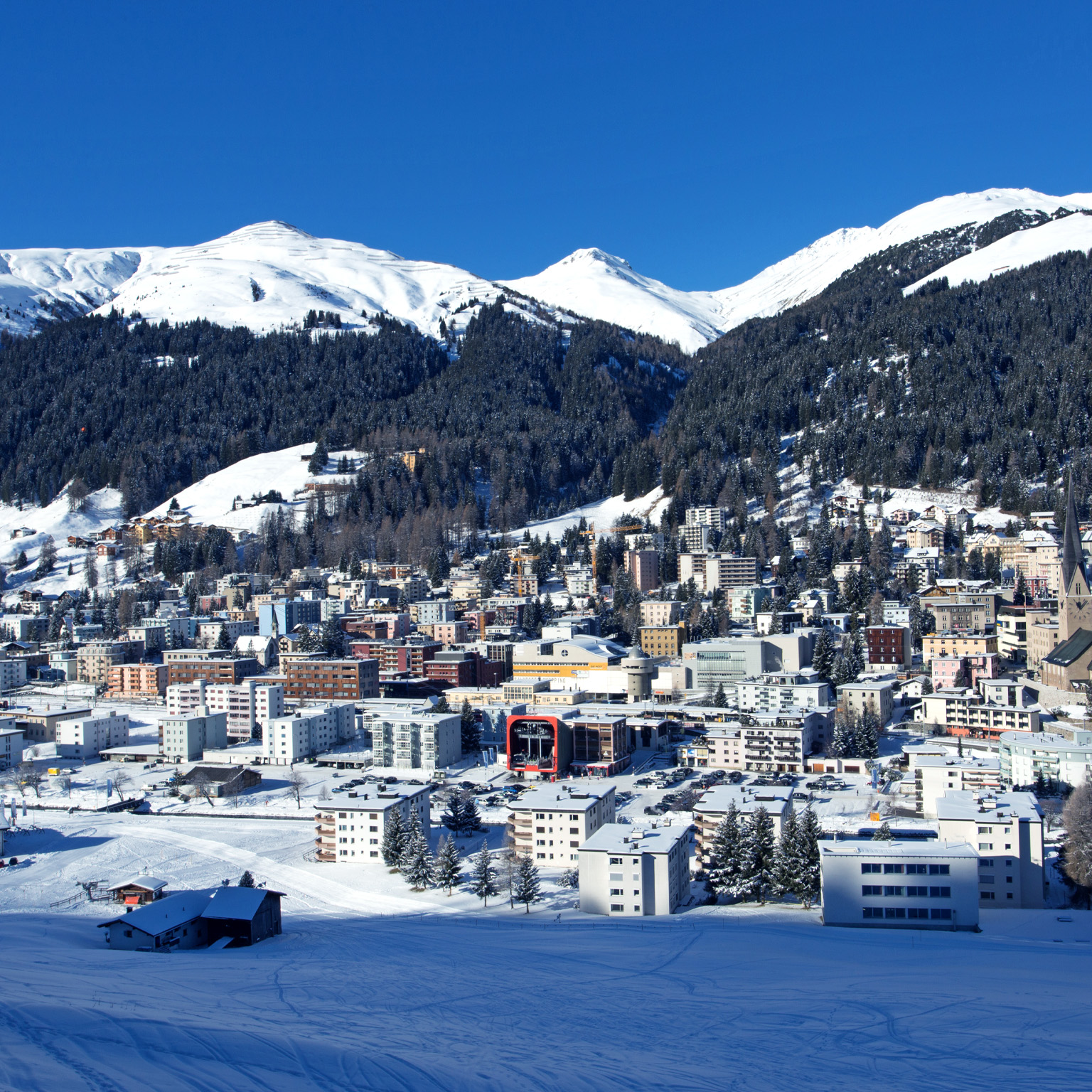 On a bright winter day, Davos, Switzerland can be seen from above, with a snowy landscape and the Schtzalp mountain in the distance.