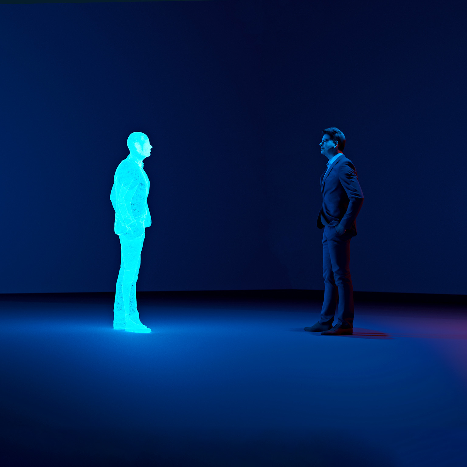 Man stands in a room looking at an avatar of himself. The clone is shown as a hologram.