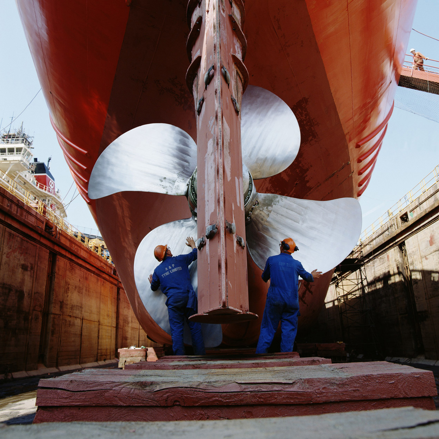 The image captures workers performing maintenance on a large ship's propeller and rudder in a dry dock. This process involves essential inspections and upkeep.