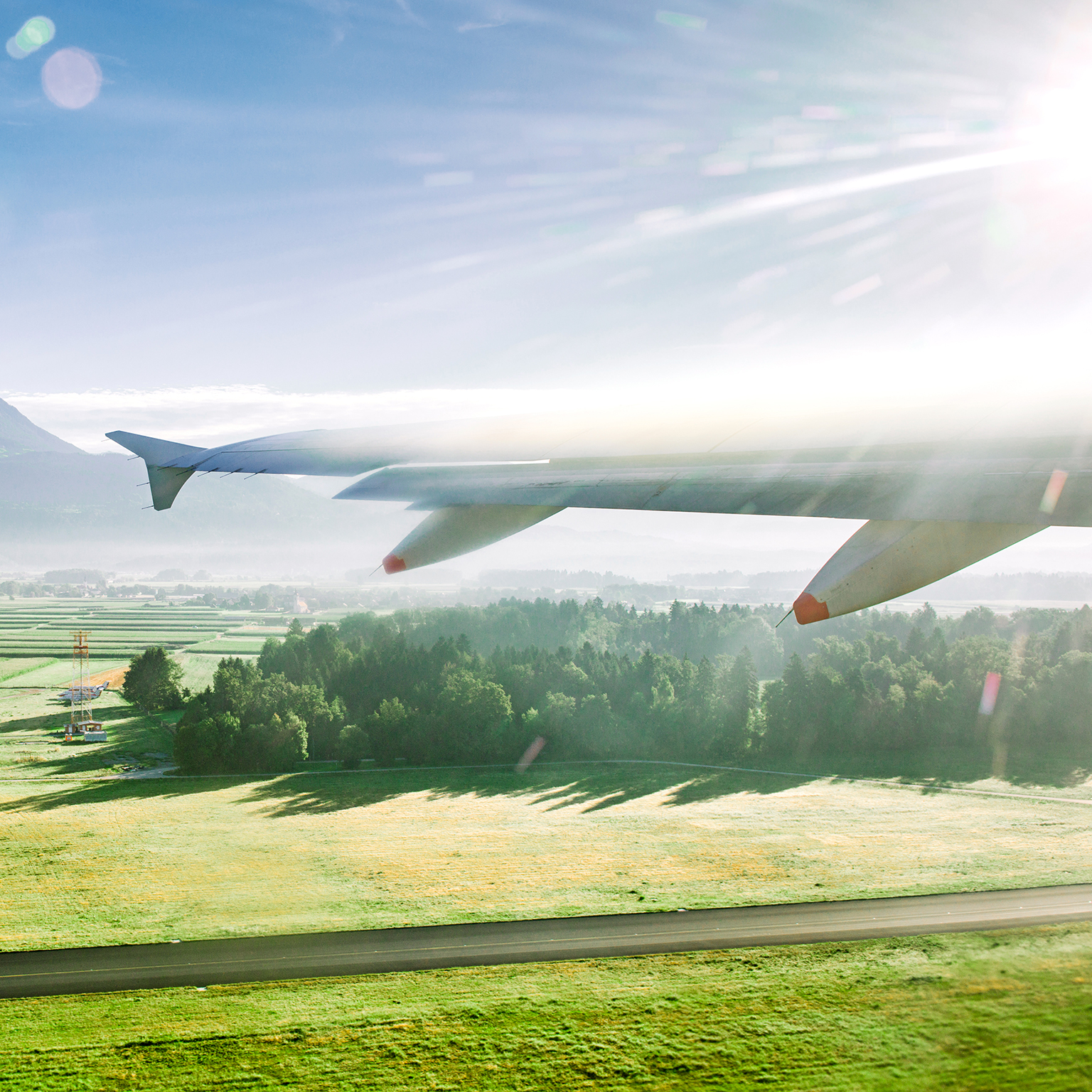 View of lush green fields outside plane window as wing flies forward.